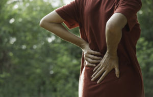 An elderly woman holding her lower back because she's experiencing pain.