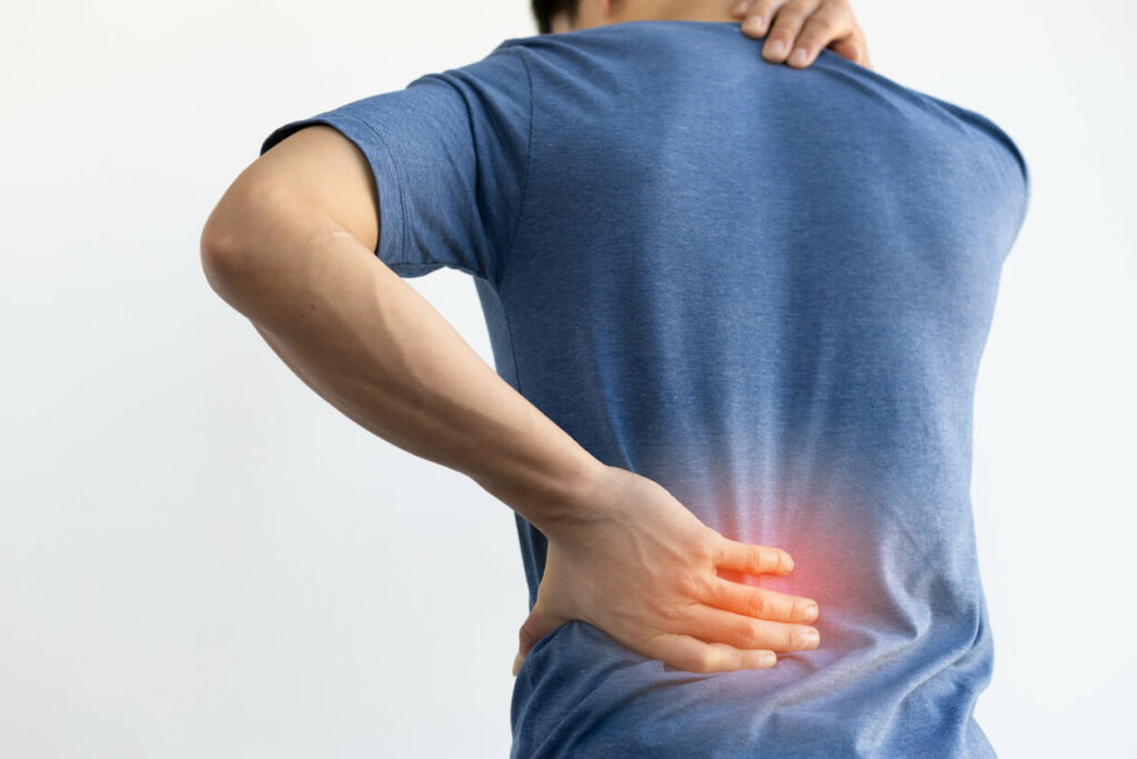 A photo showing the back of a man wearing a blue shirt who is experiencing chronic back pain.