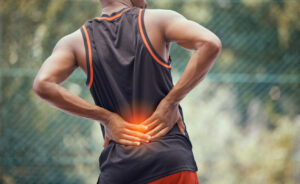 An athletic fit man outdoors is holding and massaging his lower back due to tired and strained muscles.
