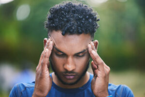 A man experiencing headache symptoms after a workout in nature, possibly a concussion.