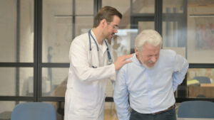 A pain management doctor is examining an elderly man with back pain.