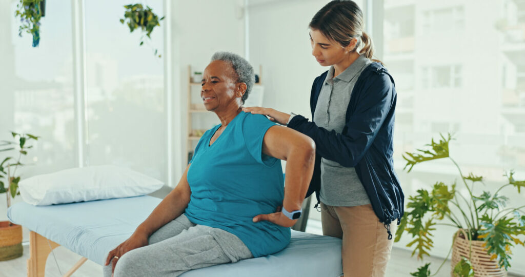 A chiropractor is consulting with old woman in clinic for chiropractor care for back pain.