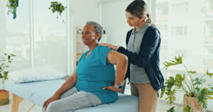 A chiropractor is consulting with old woman in clinic for chiropractor care for back pain.