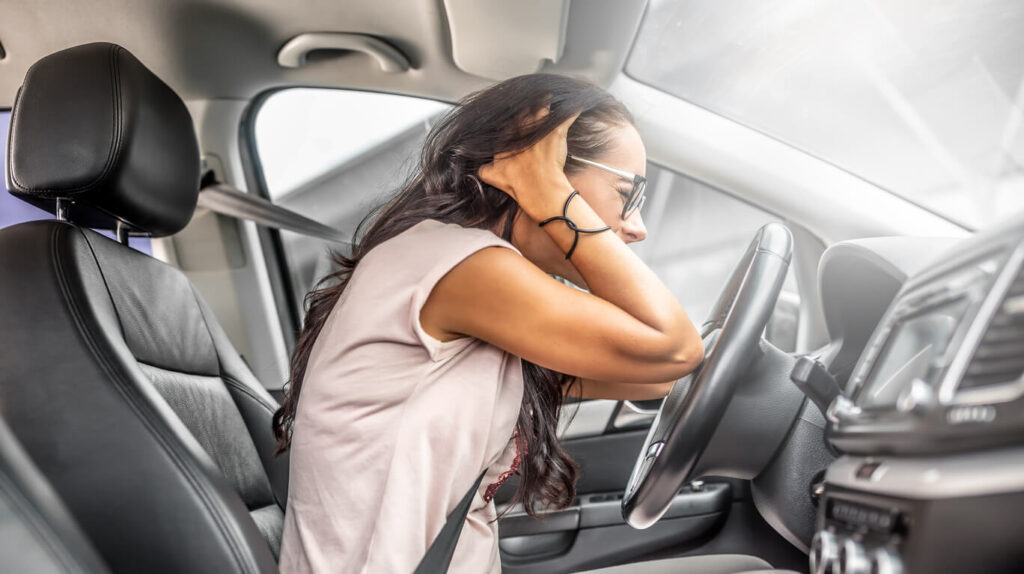 Female driver with headache or in desperation holds her head with both hands sitting on a driver's seat, after a car accident.